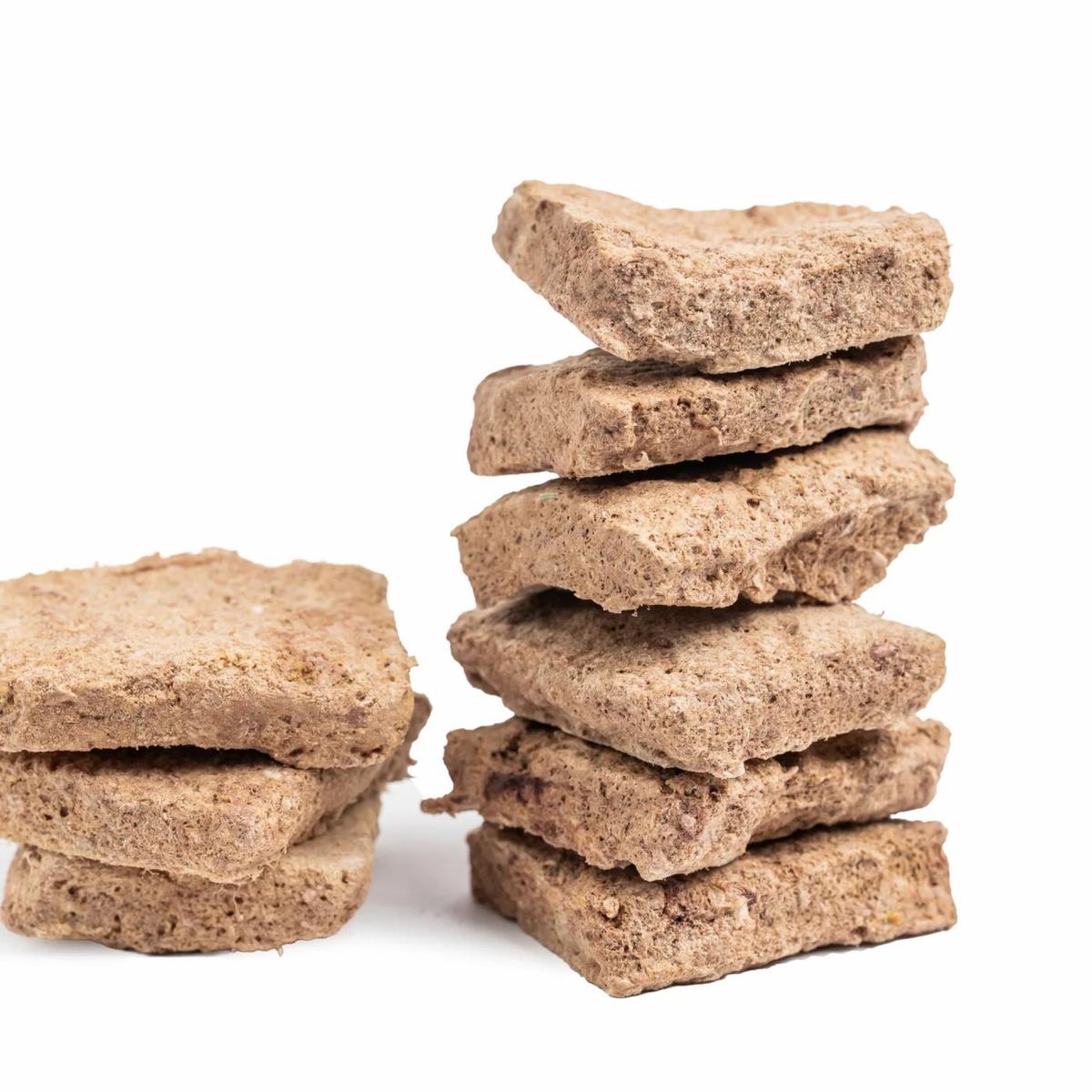 Two stacks of square, textured brown dog treats made from whole grain or wheat, photographed on a clean white background.