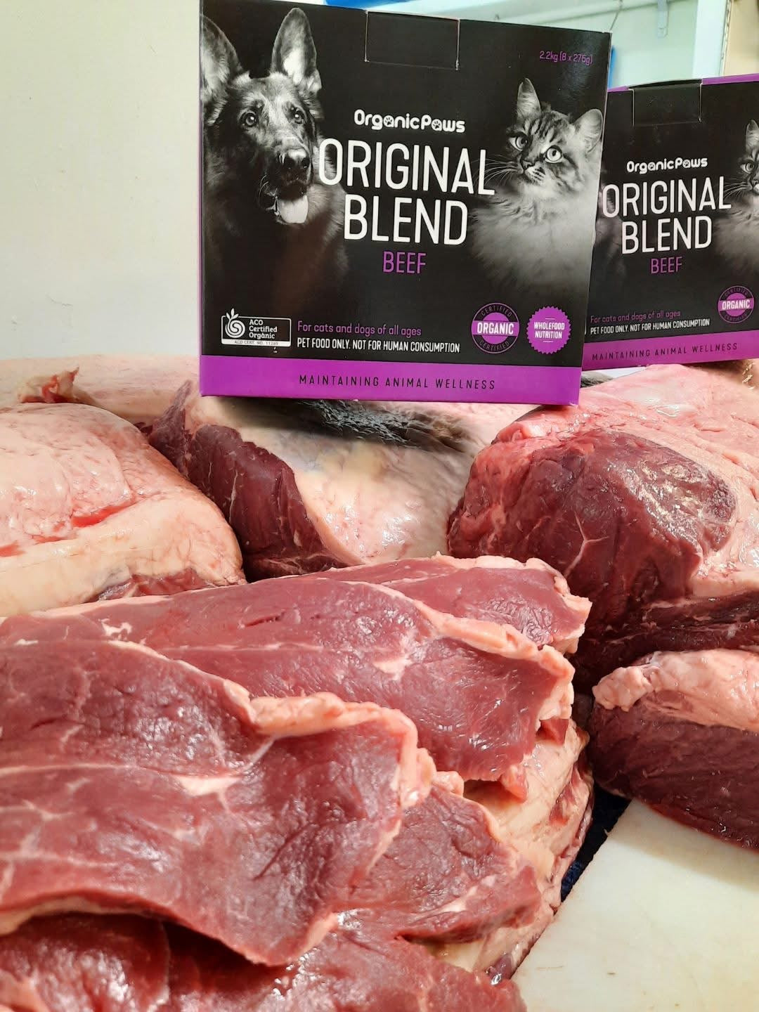 Raw beef meat with Organic Paws Original Blend Beef pet food packaging in the background.