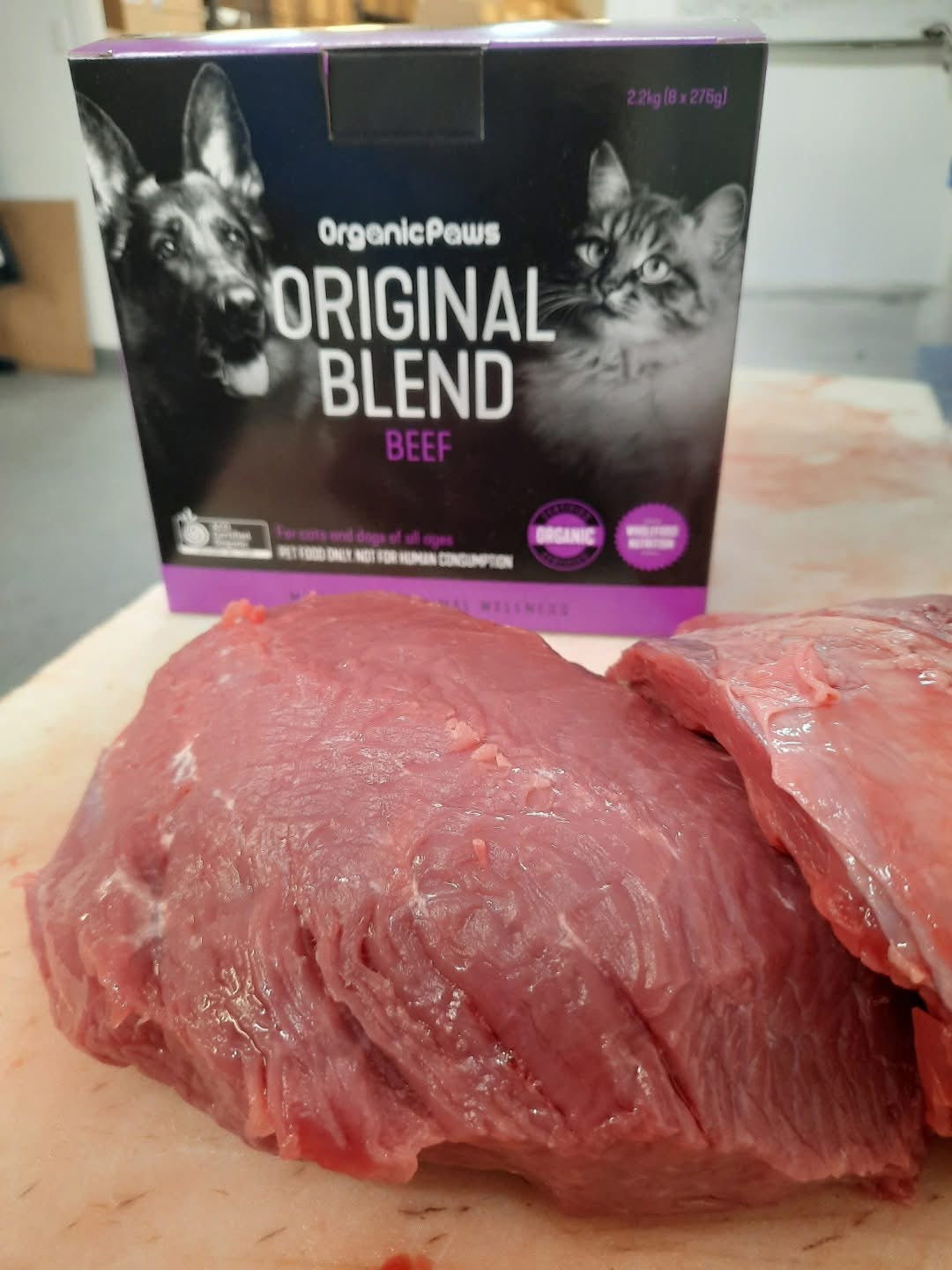 Box of Organic Paws Original Blend Beef cat food on a cutting board with raw meat.