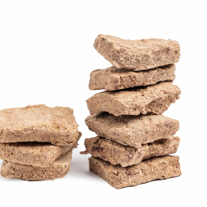 Two stacks of square, textured brown dog treats made from whole grain or wheat, photographed on a clean white background.